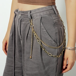 Detail of a layered golden metal waist chain with ball charms on grey denim pants