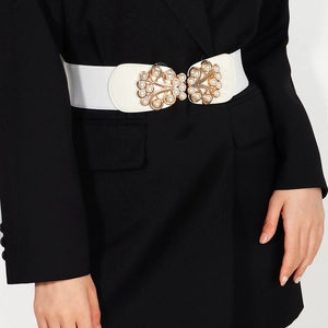 Detail of white elastic waist belt with gold buckle and pearls on a black blazer