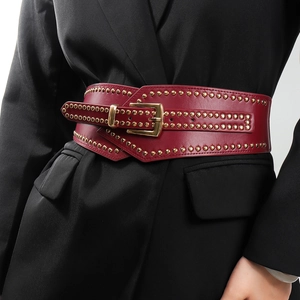 Detalle de cinturón corsé de cuero burdeos con tachuelas doradas sobre blazer negro