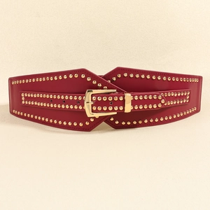 Detalle de cinturón corsé de cuero rojo con tachuelas doradas y hebilla rectangular