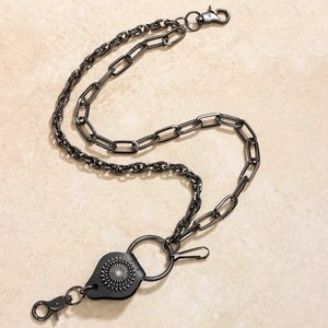 Detail of punk style black layered metal pants chain with leather sunburst charm
