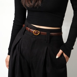 Close-up of a slim dark brown leather belt with a golden oval buckle on black trousers