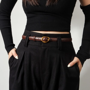 Detail of slim dark brown leather belt with gold oval buckle on black pleated trousers