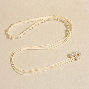 Dettaglio catena in vita in pelle intrecciata crema con perle bianche e oro brillante
