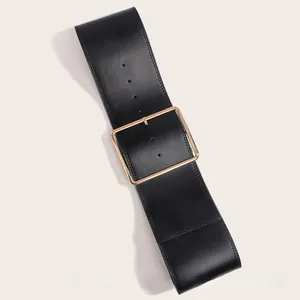 Détail d'une large ceinture noire en similicuir avec boucle carrée dorée et perforations