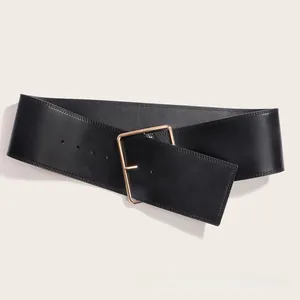 Détail d'une large ceinture en cuir noir avec une grande boucle carrée dorée et polie