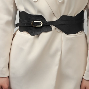 Détail d'une ceinture corset noire avec boucle dorée portée sur un blazer beige