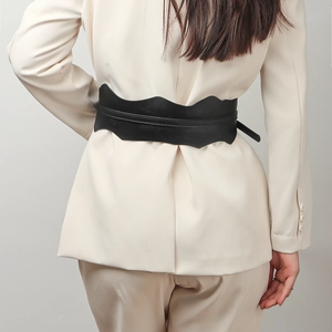 Détail d'une ceinture corset noire en similicuir à bords ondulés sur une veste beige
