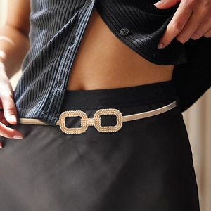 Détail d'une fine ceinture en métal doré avec boucle à double anneau texturée sur noir