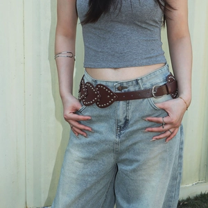 Détail d'une ceinture en cuir marron avec rivets en forme de cœur sur un jean bleu