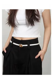 Detail of white slim waist belt with golden 3D rose buckle on black pants and top