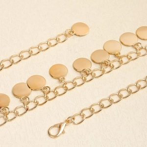 Détail d'une chaîne de taille en métal doré poli avec pendentifs disques et fermoir mousqueton