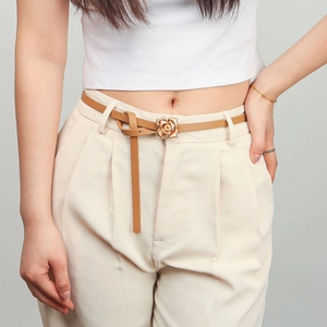 Detail of a thin tan leather belt featuring a golden rose flower buckle on white pants