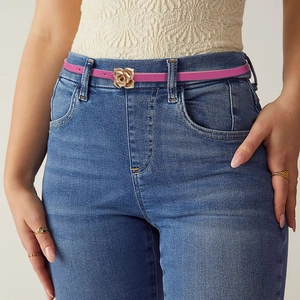 Detail of a pink skinny belt featuring a golden rose-shaped buckle on denim jeans