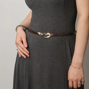 Close-up of a slim brown leather belt with a gold heart buckle on a grey dress