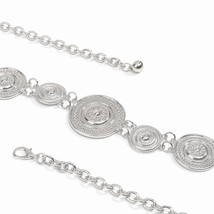 Close-up of silver chain belt showing sunburst relief pattern on circular plates