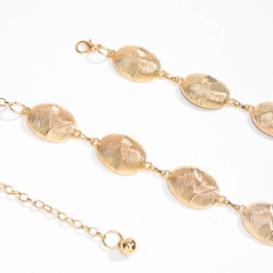 Detail view of golden oval chain belt showing intricate radial engraved texture and clasp