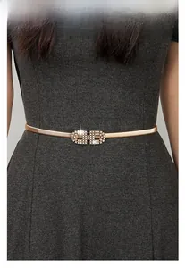 Détail d'une ceinture métallique dorée élastique avec boucle à double anneau en strass