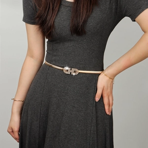 Détail de la ceinture fine en chaîne dorée avec boucle rectangulaire ornée de strass