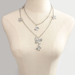 Détail du collier argenté double couche avec des breloques papillon et des pompons