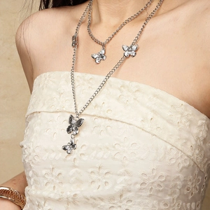 Détail d'un collier multicouche en métal argenté avec papillons sur robe en dentelle