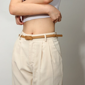 Détail d'une fine ceinture en cuir marron pour femme avec boucle carrée sur pantalon beige