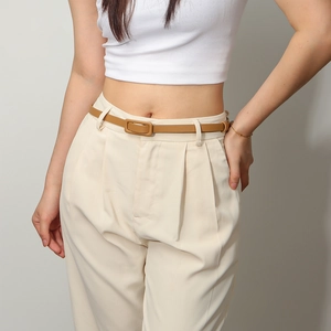 Détail d'une fine ceinture marron clair avec boucle rectangulaire sur un pantalon beige