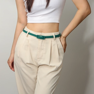 Détail d'une fine ceinture vert vintage avec boucle assortie sur un pantalon beige