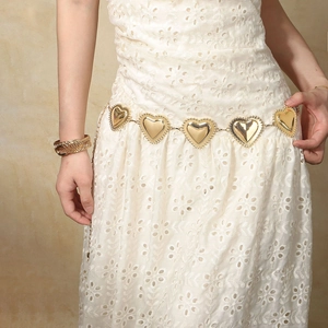 Ceinture chaîne dorée avec pendentifs en cœur sur une robe d'été blanche en dentelle