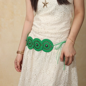Detail of green leather disc belt with turquoise studs on white lace dress