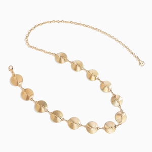 Detail of golden metal waist chain featuring round plates with spiral textured patterns