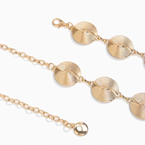 Macro detail of golden metal waist chain featuring round spiral textured medallions