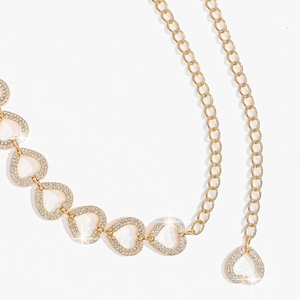Détail d'une chaîne de taille dorée avec pendentifs cœur évidés et strass brillants