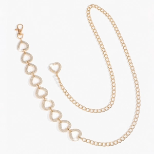 Détail d'une chaîne de taille dorée en forme de cœur avec des strass brillants sur blanc