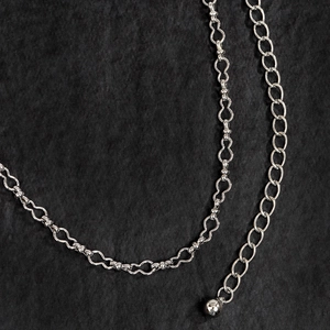 Dettaglio ravvicinato di una catena da vita in metallo argento con maglie ondulate e ciondolo