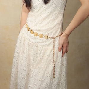 Detail of a polished gold metal chain belt with round links on a white lace dress