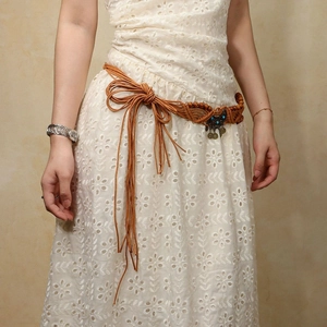 Detail of bohemian woven waist belt with tassels, beads and vintage metal pendant