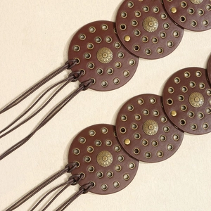 Makroaufnahme von braunen Lederscheiben mit Sonnenstrahl-Metallnieten auf dem Gürtel