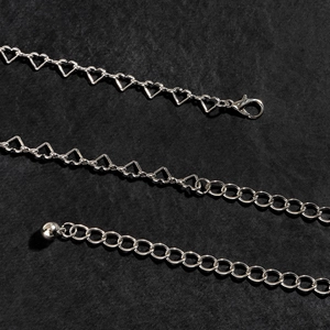 Catena in metallo argento con maglie a cuore e a V su sfondo di pelle nera