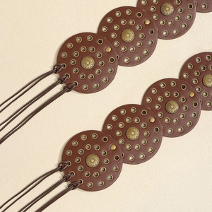 Detail of vintage brown leather belt with circular cutouts and floral metal studs