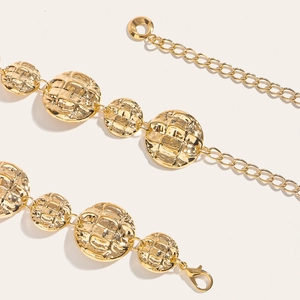 Detailed close-up of golden metal belt with textured round plates and lobster clasp