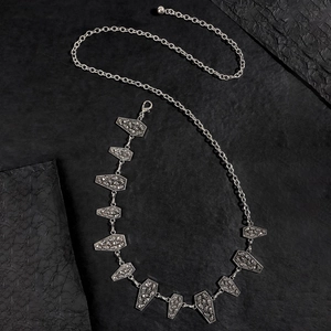 Macro detail of silver gothic waist chain with coffin charms and skull engravings