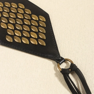 Detail of black leather belt with bronze leaf rivets and suede tassels in punk style