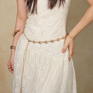 Detail of elegant gold metal waist chain with circular cutouts on a white dress