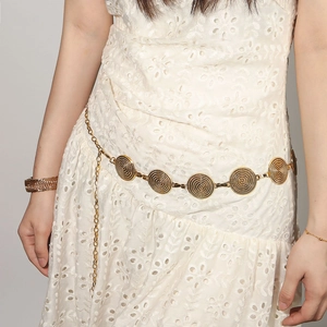 Détail d'une chaîne de taille dorée rétro avec disques en relief sur une robe blanche