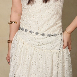 Close-up of a silver metal waist chain with circular charms on a white lace dress