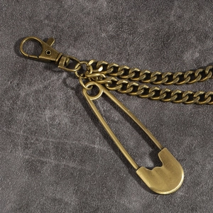 Macro detail of vintage bronze pants chain featuring a safety pin and dual curb chains