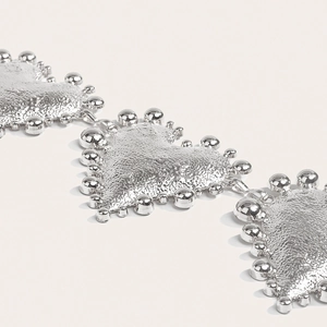 Close-up of heart-shaped metal charms with hammered texture and beaded edges in silver