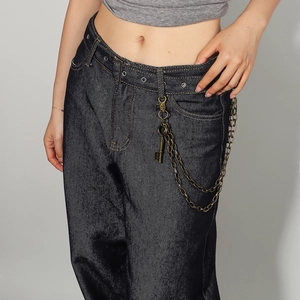 Detail of vintage metal waist chain with feather charms on dark blue washed denim jeans