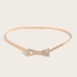 Détail d'une ceinture dorée à maillons avec boucle en forme de nœud sertie de strass
